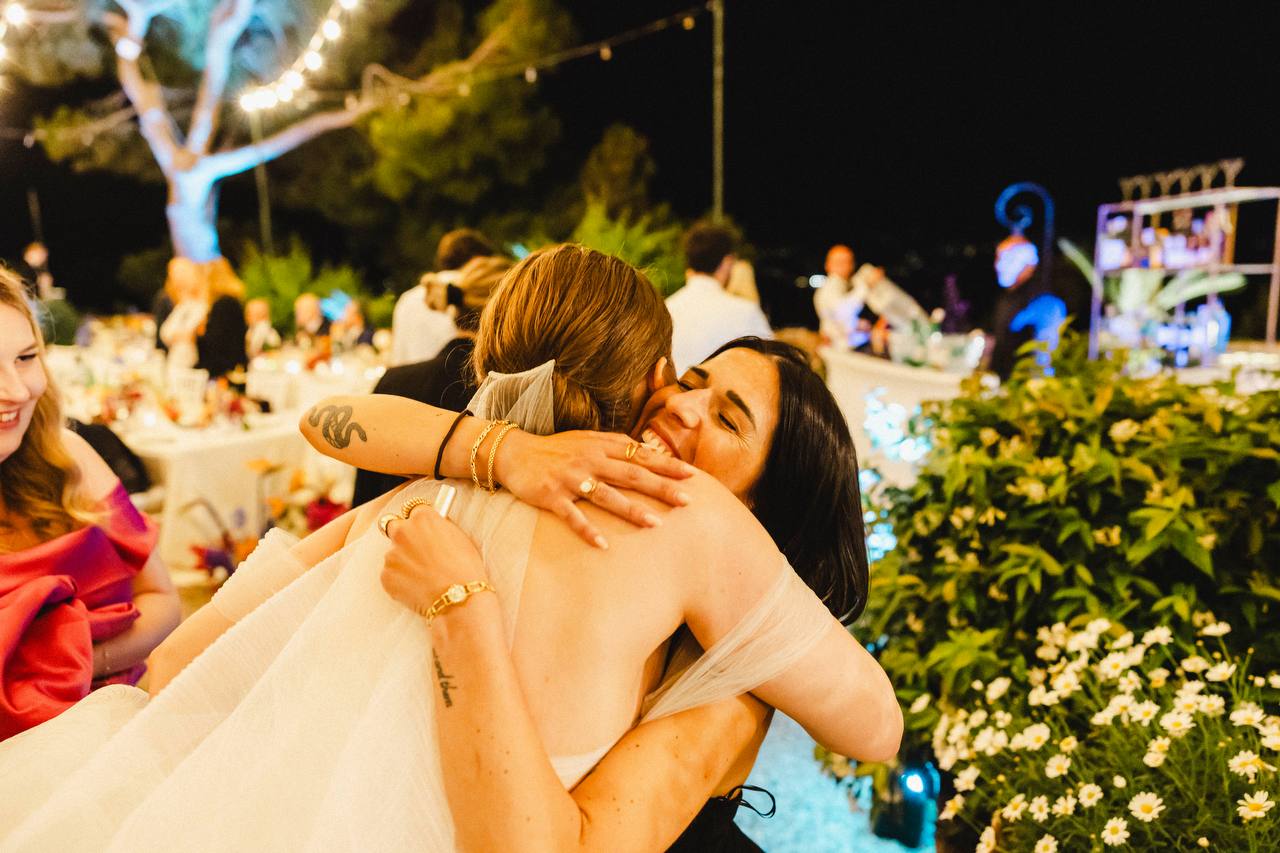 Due donne che si abbracciano durante un evento serale all’aperto in La mia famiglia lavorativa